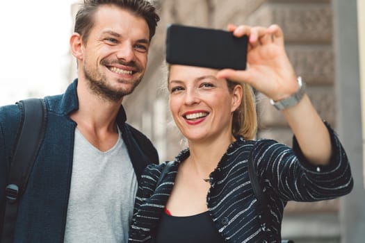 Young millennial couple living in the city, taking a selfie with a smart phone.