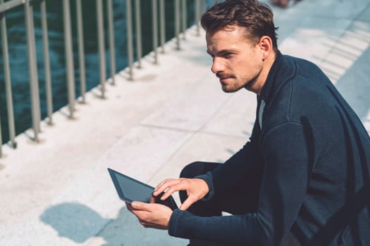 Beautiful caucasian man living in the city. Man spending his day in the city, sun is shining, weather is nice. Young millennial person living in the city, doing his daily errands always using his digital devices, tablet or phone.