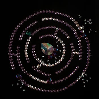 Rhinestones in the form of a labyrinth with a flat lay, isolated on a black background. Top view pattern or labyrinth of rhinestones in lilac and silver color