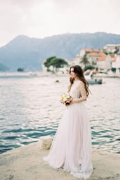 Bride with a bouquet stands on the pier near the coast of Perast. High quality photo