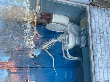 Skeleton sitting on a toilet wearing a mask in store window display. High quality photo