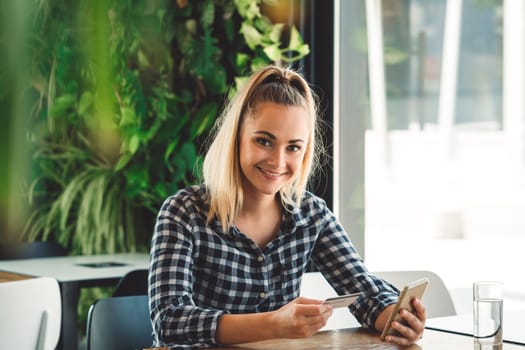 Young caucasian person using a wireless payment method. Young person holding her credit card next to a card reader, paying for her coffee.