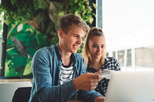 Young caucasian couple of students sitting at a cafe online shopping on their laptop. Both smiling while looking at the laptop.