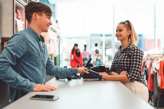 Young caucasian person using a wireless payment method. Young person holding her credit card next to a card reader, paying for her coffee.