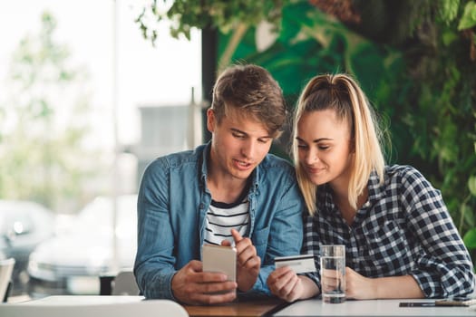 Young caucasian couple of students sitting at a cafe online shopping on their laptop. Both smiling while looking at the laptop.