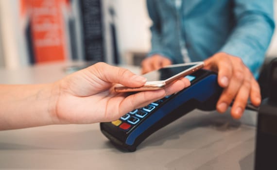 Young caucasian person using a wireless payment method. Young person holding her credit card next to a card reader, close up.