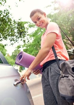 Looking forward to this yoga class. a beautiful young woman carrying a yoga mat while getting into her car