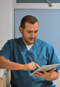 Looks like I have a full day today. a cheerful young male dentist working on his laptop while standing in his office