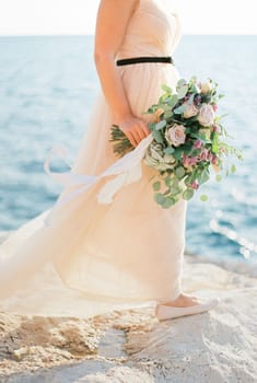 Bouquet of flowers in the bride hand on a stone seashore. High quality photo