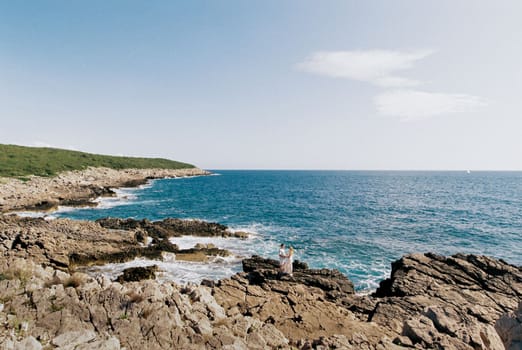 Man and woman stand on rocks holding hands near blue water. High quality photo