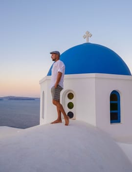 Young men watching the sunrise in Santorini Greece, man on vacation at the Greek village Oia with whitewashed house and churches.