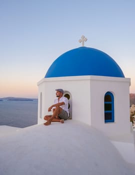 Young men watching the sunrise in Santorini Greece, man on vacation at the Greek village Oia with whitewashed house and churches.