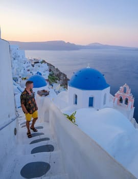 Young men watching the sunrise in Santorini Greece, man on vacation at the Greek village Oia with whitewashed house and churches.