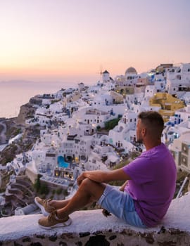 Young men watching the sunrise in Santorini Greece, man on vacation at the Greek village Oia with whitewashed house and churches.