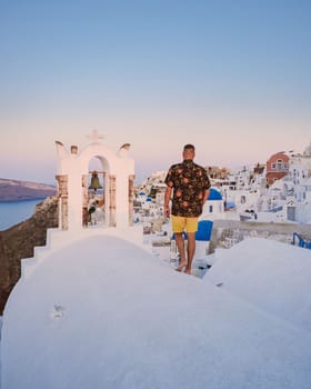 Young men watching the sunrise in Santorini Greece, man on vacation at the Greek village Oia with whitewashed house and churches.