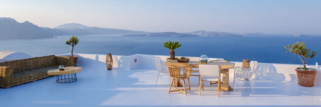 outside terrace of a restaurant by the ocean of Santorini Greece, chairs, and tables with flowers by the ocean.