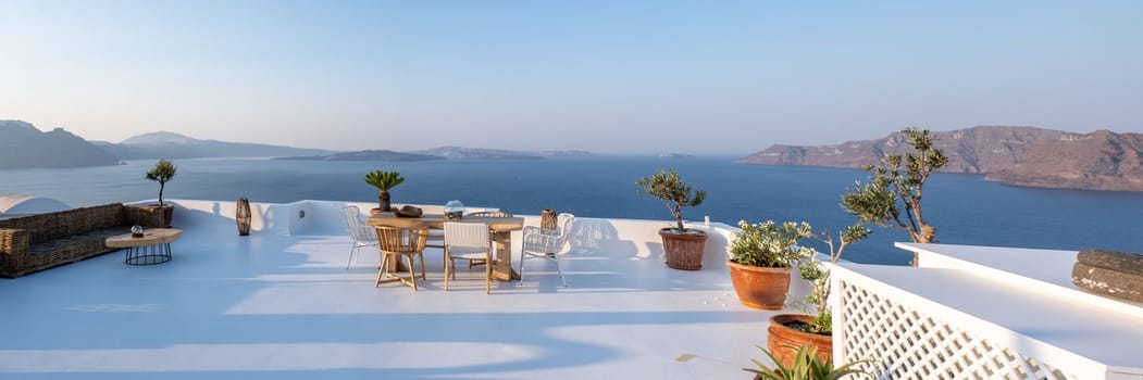 outside terrace of a restaurant by the ocean of Santorini Greece, chairs, and tables with flowers by the ocean.