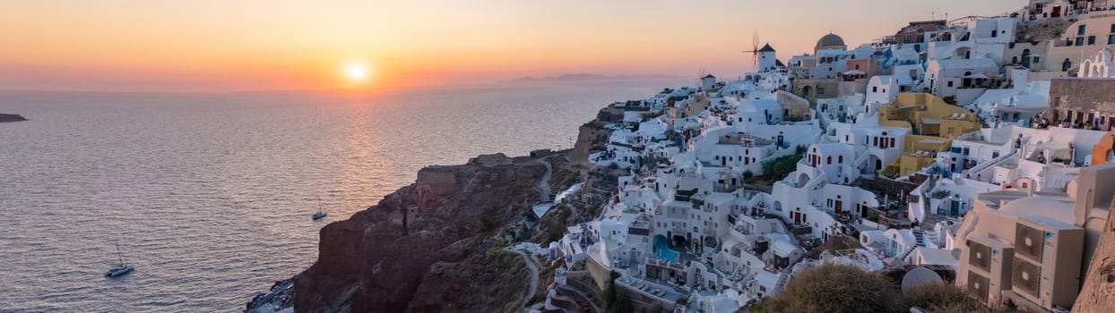 Sunset with white churches an blue domes by the ocean of Oia Santorini Greece.