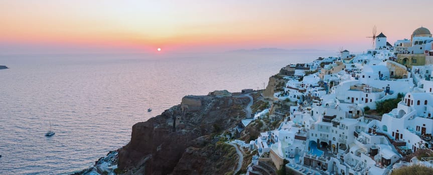 Sunset with white churches an blue domes by the ocean of Oia Santorini Greece.