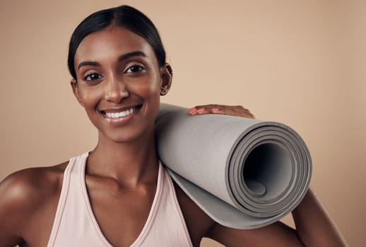 I incorporate yoga into my routine. an attractive young woman standing alone in the studio and holding a yoga mat