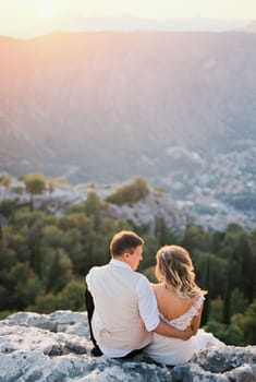 Bride and groom are sitting on the top of the mountain and looking at the valley. High quality photo