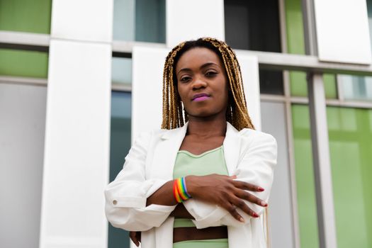 Young African American woman standing outdoors with arms crossed wearing rainbow bracelet. LGTBQ concept.
