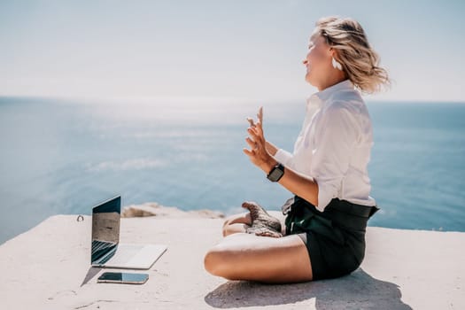 Happy girl doing yoga with laptop working at the beach. beautiful and calm business woman sitting with a laptop in a summer cafe in the lotus position meditating and relaxing. freelance girl remote work beach paradise