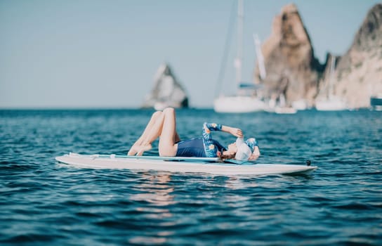 Woman sup yoga. Middle age sporty woman practising yoga pilates on paddle sup surfboard. Female stretching doing workout on sea water. Modern individual hipster outdoor summer sport activity