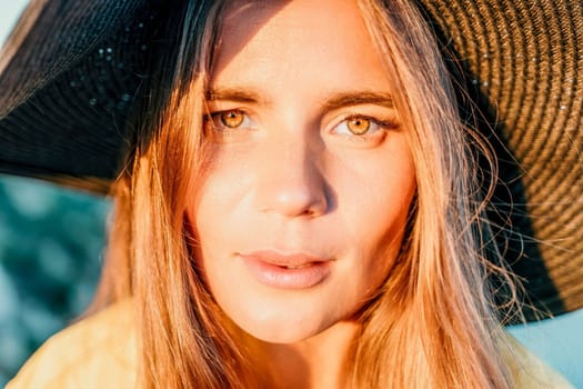 Portrait of happy young woman wearing summer black hat with large brim at beach on sunset. Closeup face of attractive girl with black straw hat. Happy young woman smiling and looking at camera at sea