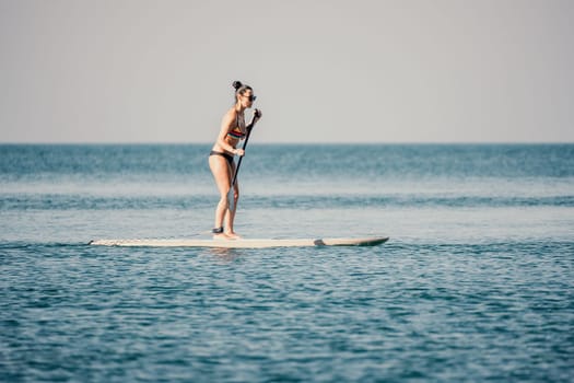 Sea woman sup. Silhouette of happy middle aged woman in rainbow bikini, surfing on SUP board, confident paddling through water surface. Idyllic sunset. Active lifestyle at sea or river