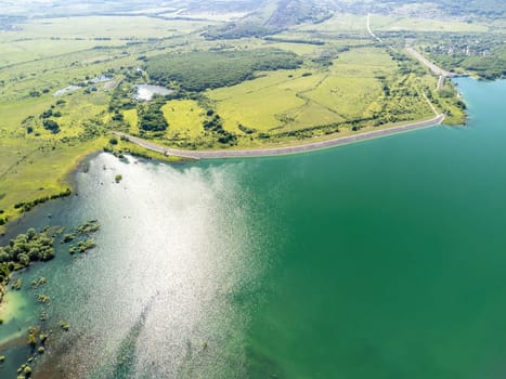 Aerial landscape from flying drone storage reservoir at mountain foot covered colorful spring forest. Beautiful view from above blue lake among highlands