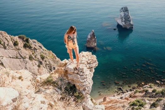 Woman travel sea. Happy tourist taking picture outdoors for memories. Woman traveler looks at the edge of the cliff on the sea bay of mountains, sharing travel adventure journey.