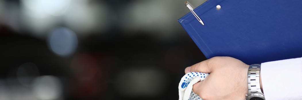 Car mechanic priemchik holds gloves and clipboard in car service. Car insurance and maintenance after a breakdown or accident