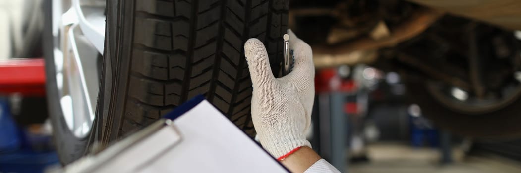 Man mechanic working under car at car service station. Experienced mechanic examines car tires