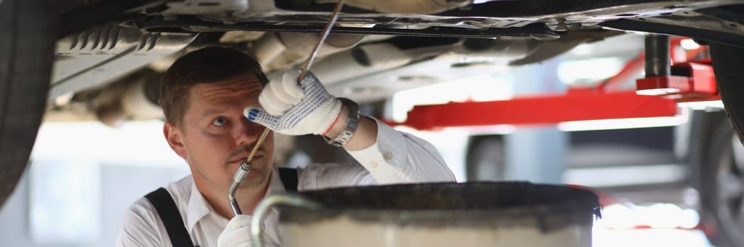 Auto mechanic checks running gear of car and oil leak at service station. Male worker fixing breakdown problem with a machine