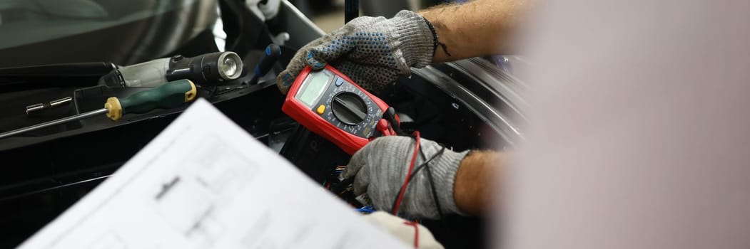 Mechanical service using multimeter to check voltage level in car battery and auto documentation diagram. Car diagnostics in car service
