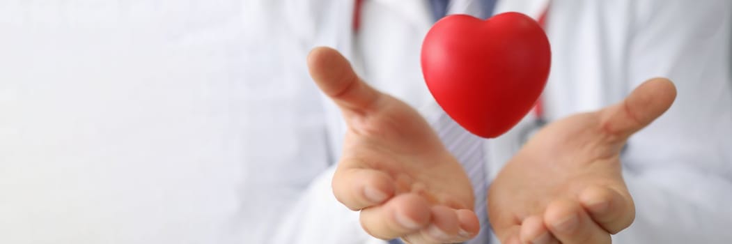 Doctor cardiologist holds hands and airborne red toy heart closeup. Cardiotherapist and treatment of heart diseases