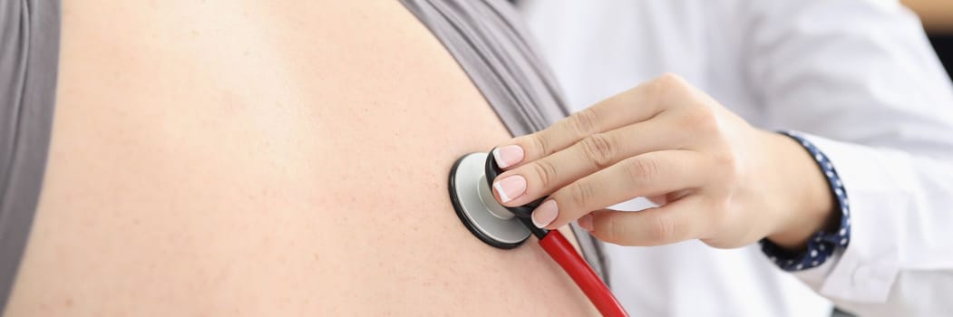 Female doctor listens to man back through astethoscope. Inflammation of lungs and painful cough