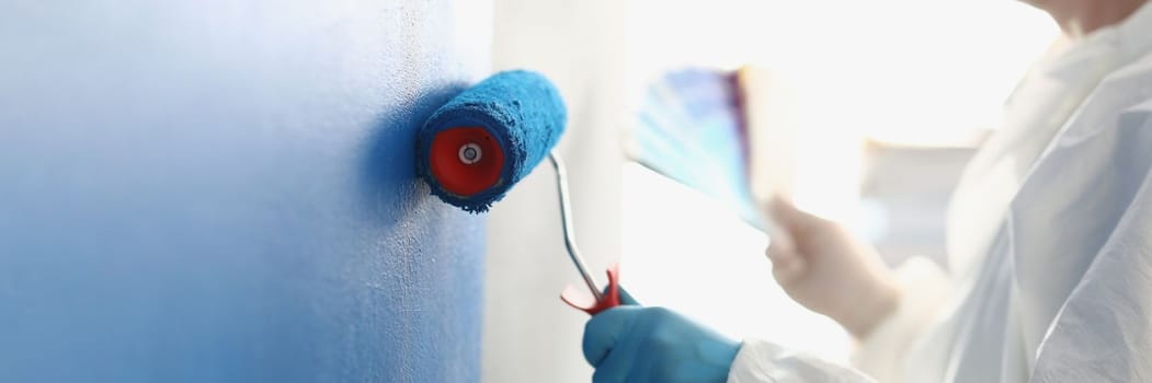 Painting white wall with blue roller. Services of master painter for home repair