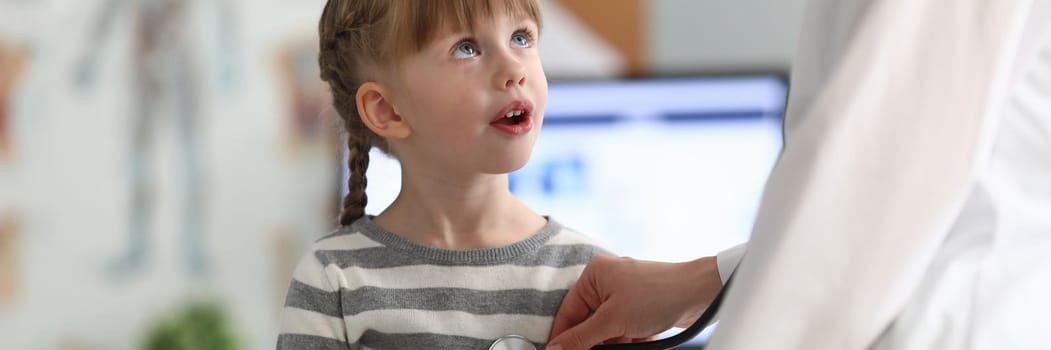 Smiling girl at doctor office in clinic. Female pediatrician examining small child with a stethoscope