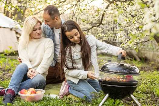 Happy girl, father and mother preparing barbecue in the yard.