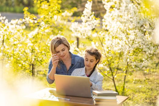 Mother daughter spending time outside. Mom and kid using laptop in nature.