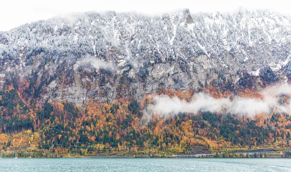 Snow covered the mountain beside Thun lake in autumn. The trees changing color from green to orange in Interlaken, Switzerland.