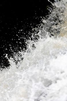 Close focus on splashing water of waterfall with dark background.