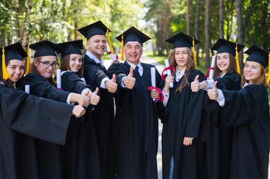 A group of graduates in robes give a thumbs up outdoors. Elderly student