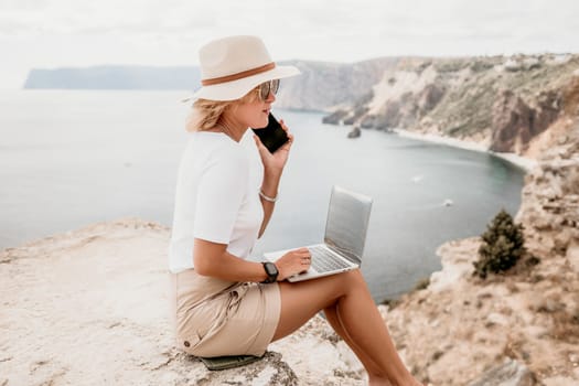 Digital nomad, Business woman working on laptop by the sea. Pretty lady typing on computer by the sea at sunset, makes a business transaction online from a distance. Freelance remote work on vacation