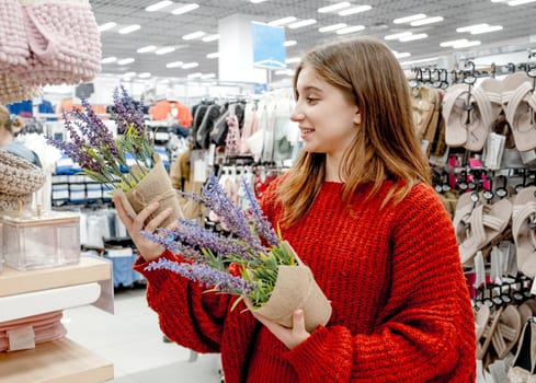 Pretty girl choosing artificial lavander flower for home decoration in supermarket. Beautiful female teenager buying plants in shopping center mall