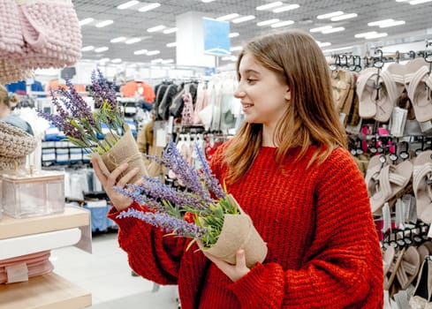 Pretty girl choosing artificial lavander flower for home decoration in supermarket. Beautiful female teenager buying plants in shopping center mall