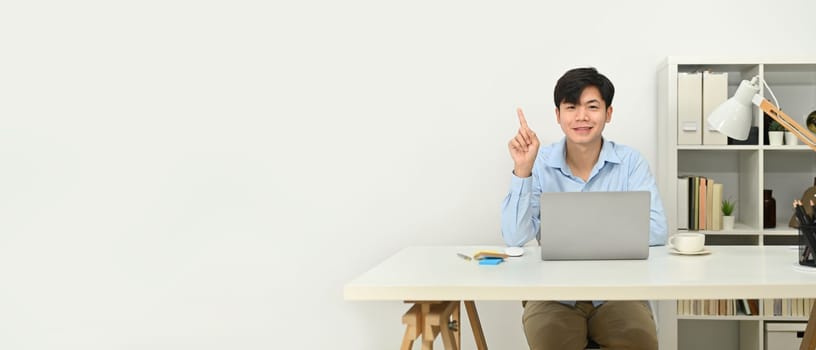 Smiling handsome businessman sitting front of laptop and pointing at copy space for text. Horizontal banner.