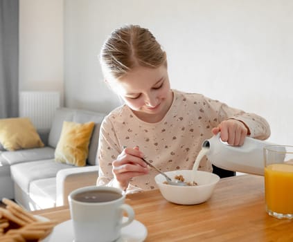 Cute girl child put milk to plate with cereal oat meal for breakfast. Female kid with musli food and latte during morning nutrition